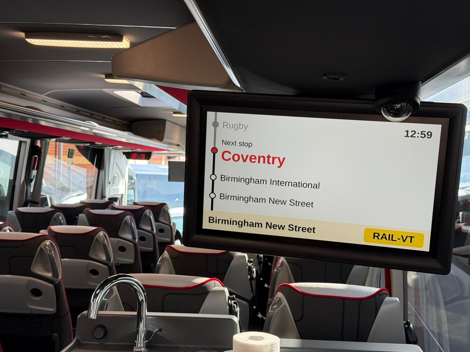 Inside an Alpha AIR-equipped coach: rows of passenger seats and the next-stop screen reading Next stop Coventry.